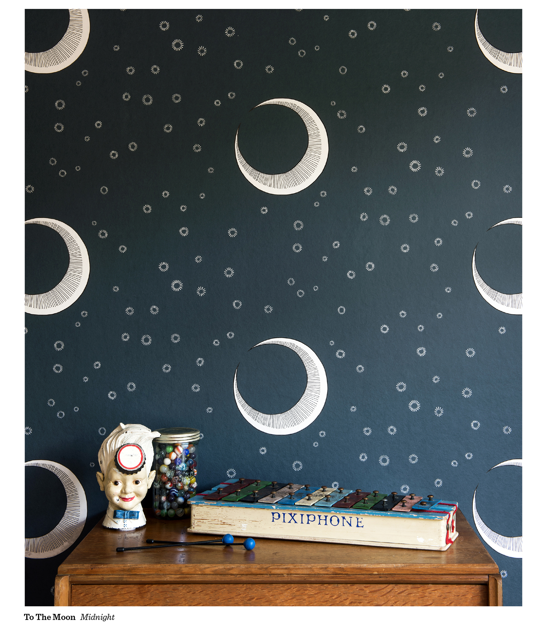 MissPrint To The Moon wallpaper in Midnight, with cream crescent moons and starbursts on a dark navy background, above a wooden chest of drawers